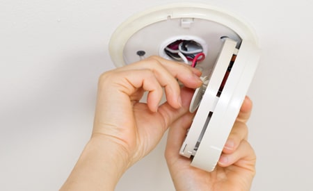 hands installing a fire alarm and smoke detector on the ceiling