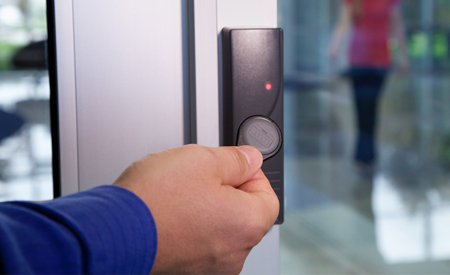 a hand holding a key fob over the access control panel