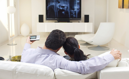 a couple sitting on the couch watching a movie with their surround sound on