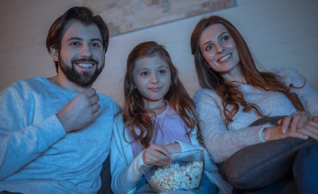 a family eating popcorn on the couch watching a movie in the dark